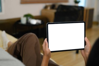 Kanepede boş bir ekranla dijital tableti tutan ellerin yakın çekimi.