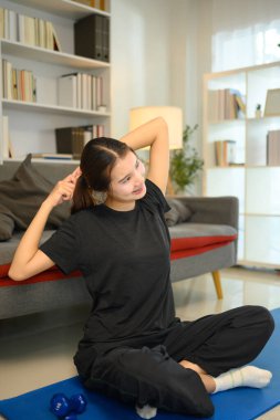 Oturma odasında yoga minderinin üzerinde gerinen neşeli Asyalı genç kadın..