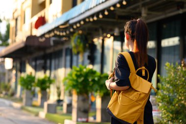 Sarı sırt çantalı genç bir turist gündüz vakti şehir caddesinde yürüyor..