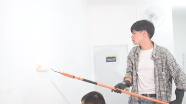 Bir ev yenileme projesi sırasında genç Asyalı bir adam paten fırçasıyla duvar boyuyor..