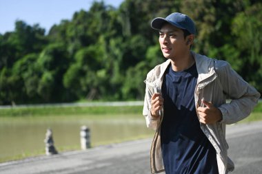 Aktif genç Asyalı adam güneşli bir günde nehir kenarında koşuyor..