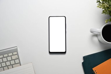 Boş akıllı telefon ekranı, klavyesi ve defterleri olan beyaz ofis masası.
