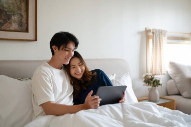 Sıcak bir yatak odasında sıcak battaniyenin altında dijital tablet kullanan sevgi dolu bir çift..