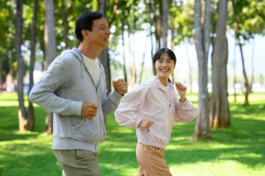 Neşeli yaşlı bir adam ve kızı güzel bir parkta asfalt bir yolda birlikte koşuyorlar..