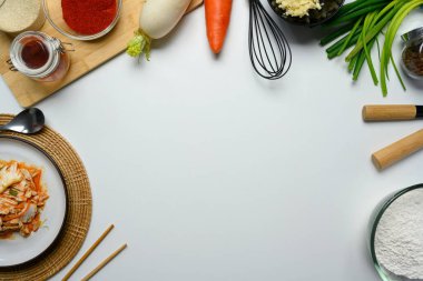 Bir tabak kimçi, temel malzemeler ve yemek çubukları beyaz arka planda. Kore mutfağı ve geleneksel meze konsepti.