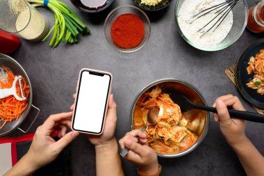 Taze malzemelerle çevrili karanlık bir tezgahta kimchi tarifi için akıllı telefonlu kadınları hazırlayan genel bakış..