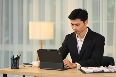 Modern ofiste dijital tablet üzerinde çalışan siyah takım elbiseli bin yıllık iş adamı..