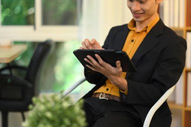 Resmi takım elbiseli yakışıklı Asyalı işadamı modern iş yerinde dijital tablet üzerinde çalışıyor..