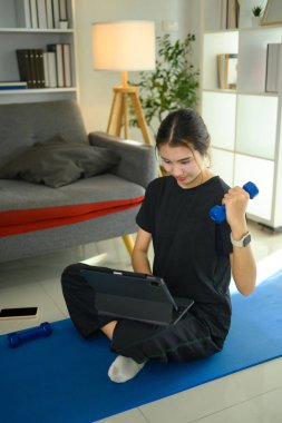 Genç Asyalı kadın halteri kaldırıyor ve yoga minderinde dijital tablet kullanıyor..