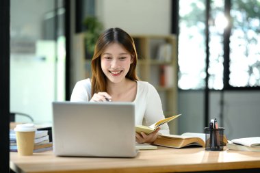 Neşeli genç kadın, parlak ve modern bir çalışma alanında dizüstü bilgisayar kullanıyor..