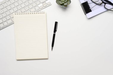 Boş not defteri, belge, klavye ve gözlükler beyaz çalışma masasında..