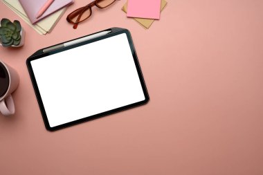 Boş ekranlı dijital tablet, bardaklar, kahve kupası ve pembe arka planda not defterleri..