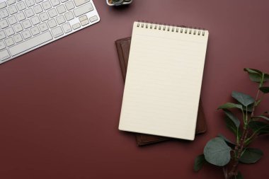 Boş bir spiral defter, klavye ve kırmızı arkaplan ile çalışma alanı.