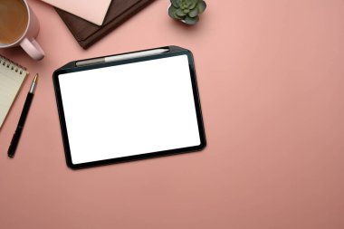 Dijital tabletli yaratıcı çalışma alanı, bir kahve fincanı ve pastel pembe yüzey üzerine not defterleri..