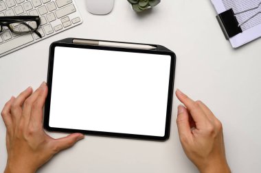 Temiz ve minimalist çalışma alanında boş beyaz ekranlı dijital tableti tutan eller.