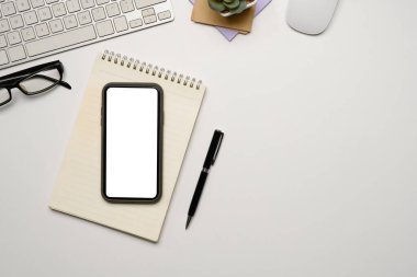 Beyaz ekranlı akıllı telefon, beyaz masada not defteri ve gözlük..