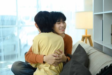 Sevgi dolu eşcinsel çift oturma odalarında sarılıyor ve güven verici bir gülümseme sergiliyor..