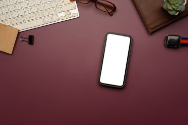 Derin kestane rengi arka planda boş ekran, klavye, gözlük ve akıllı seke sahip modern çalışma alanı akıllı telefonu.