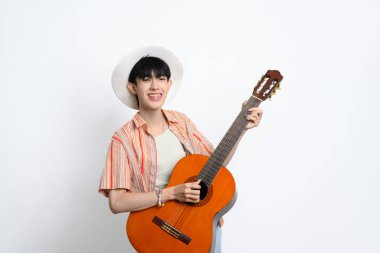 Sıradan çizgili tişört giyen, beyaz arka planda akustik gitar çalan gülümseyen genç adam..