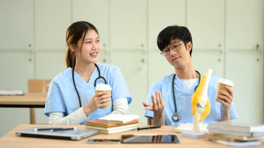 Önlüklü iki tıp öğrencisi, ders çalışırken kahve molası veriyorlar..