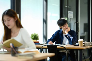 Parlak bir kütüphanede veya ortak çalışma alanında görevler üzerinde çalışan odaklanmış öğrenci.