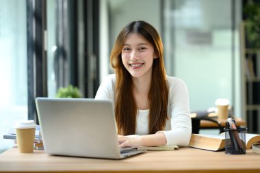 Parlak ve modern bir kütüphanede okuyan gülümseyen üniversite öğrencisi. Eğitim ve teknoloji kavramı.