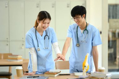 Tıp öğrencileri el ele verip masalarında kitap ve anatomik modellerle dolu bir takım çalışması yapıyorlar..