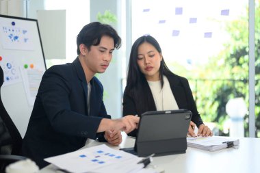 Parlak ofisteki dijital tablette gösterilen verileri analiz eden iki işadamı.