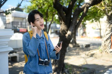 Güneşli bir şehirde cep telefonu kullanan boynunda kamera olan genç bir gezgin. Keşif ve seyahat konsepti.