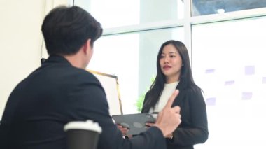 Siyah takım elbiseli kendine güvenen bir iş kadını toplantı sırasında beyaz tahtada veri sunuyor..