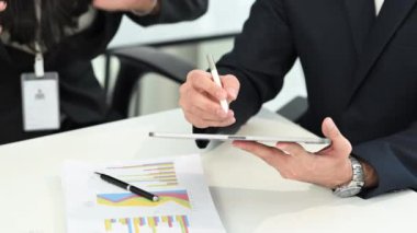 Parlak ofisteki dijital tablette gösterilen verileri analiz eden profesyonel iş adamları.
