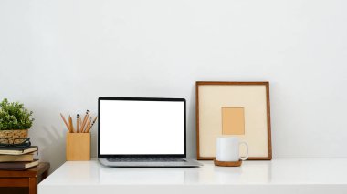 Boş ekran, kupa, resim çerçevesi ve kalem tutacağı olan bir dizüstü bilgisayarın yer aldığı minimalist çalışma alanı.