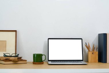 Boş ekranlı dizüstü bilgisayar, kahve fincanı, resim çerçevesi ve ahşap masadaki kırtasiye malzemesi..