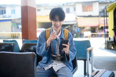 Sırt çantalı genç gezgin ulaşım terminalinde otururken akıllı telefondan seyahat planlarını kontrol ediyor..