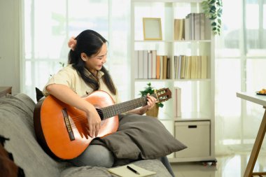 Genç, güzel bir kadın, parlak oturma odasında akustik gitar çalıyor..