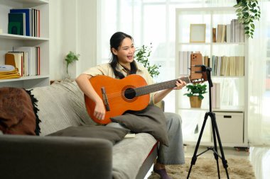 Neşeli kadın akustik gitar çalıyor ve akıllı telefonlu sosyal medya için video içeriği kaydediyor.