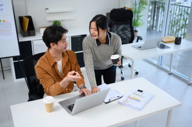 Genç iş adamları belgeleri inceliyor ve modern bir ofiste fikirleri tartışıyor..