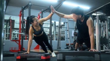 Aktif çift, spor salonunda şınav çekerken birbirlerine beşlik çakıyor..