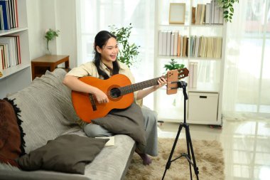 Akustik gitar çalan ve akıllı telefonlu sosyal medya için video içeriği kaydeden gülümseyen kadın.
