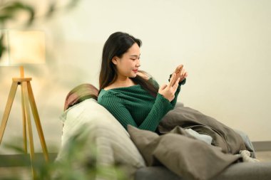 Rahat genç bir kadın kanepede oturup akıllı telefondan video izliyor..