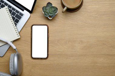 Dizüstü bilgisayarı, akıllı telefonu, kulaklığı ve kahve fincanı olan modern bir çalışma alanı manzarası..