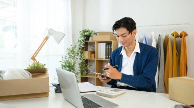 Sırıtkan genç girişimci posta kutuları ve envanter ile çevrili dizüstü bilgisayardaki emirleri yönetiyor..