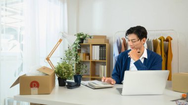 Genç girişimci, ofis masasında oturmuş bilgisayarını tamir ediyor ve hesap makinesi kullanıyor..