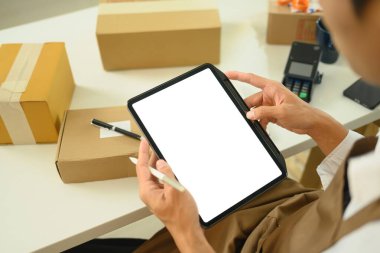 Küçük işletme sahibi dijital tablet siparişlerini yönetir ve sevkiyat için paketleri hazırlar.