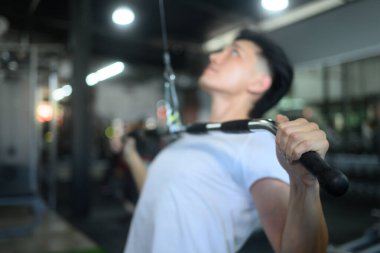 Odaklanmış adam spor salonunda kablo çekme egzersizi yapıyor, vücudunun üst kısmına odaklanıyor..