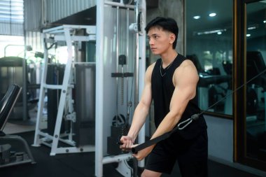 Odaklanmış bir adam spor salonunda kablo makinesiyle vücudunun üst kısmını çalıştırıyor..