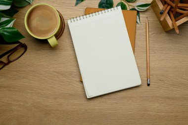 Boş not defteri, kalem, kahve fincanı, bardaklar ve ahşap masadaki yapraklı yeşillik..