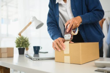 Karton kutuları paket bandıyla mühürleyen bir girişimcinin teslimat siparişini hazırlarken resmini çek..