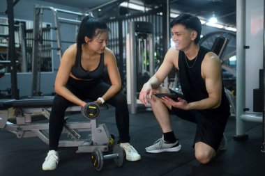 Kişisel antrenör, güç eğitimine ara verilirken bir müşteriyle çalışma planlarını gözden geçiriyor..