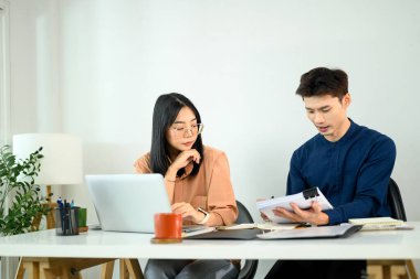 İki iş arkadaşı, finansal raporları ve proje detaylarını modern bir ofiste tartışıyor..